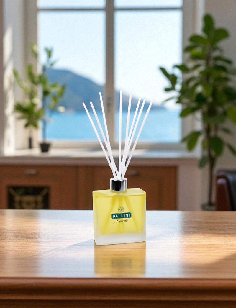 Yellow diffuser with white reed sticks on a wooden table in a room with large windows.