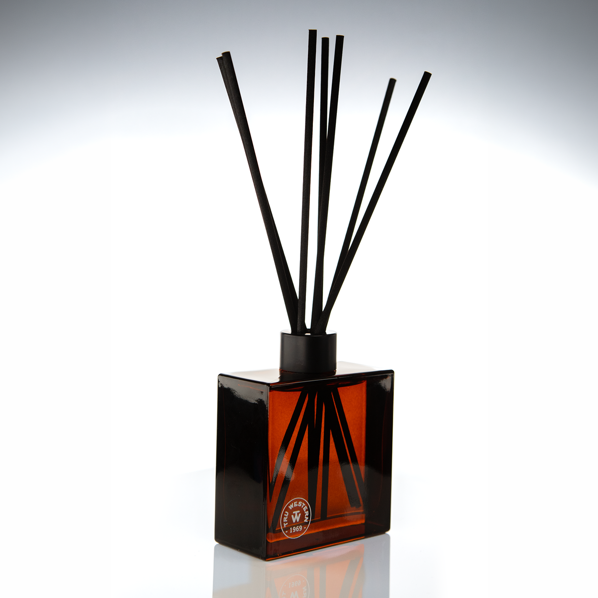 Amber glass 8 oz reed diffuser with black reeds and a seal logo on a dark gradient backdrop