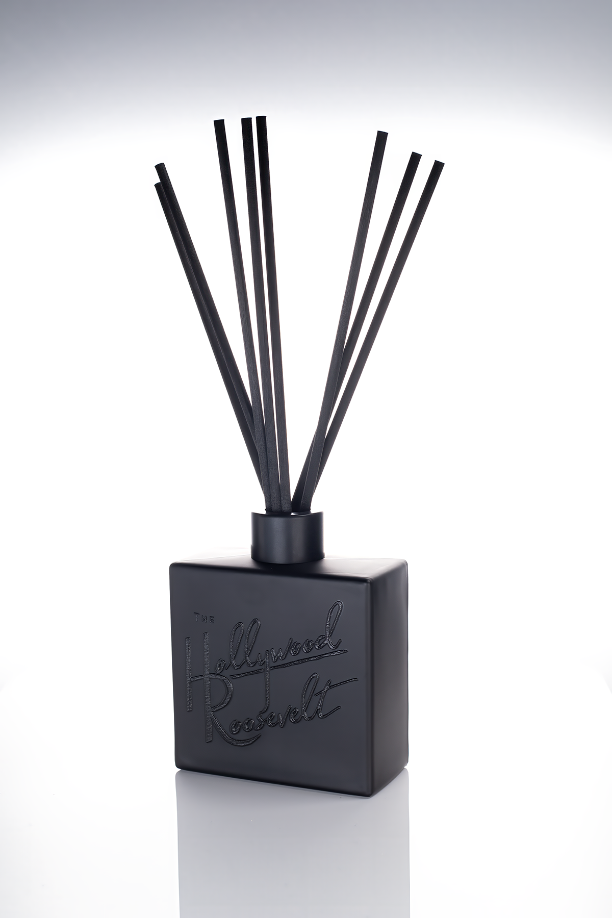 Matte black reed diffuser with black reeds and a tone-on-tone black printed script logo, on a white studio background.