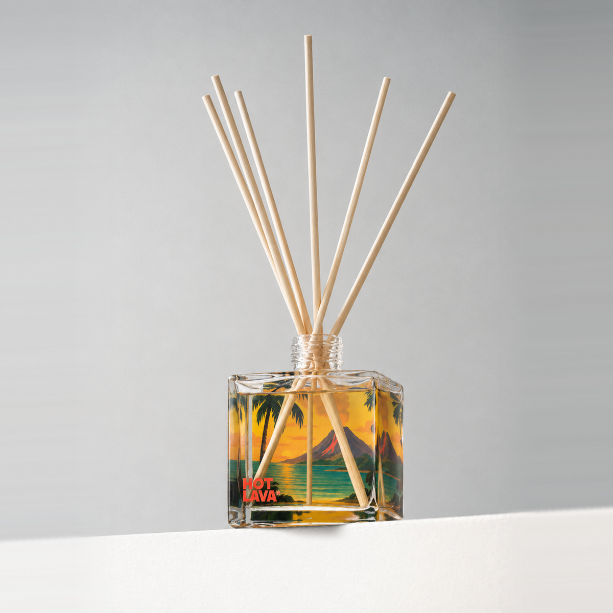 Clear glass 8 oz. reed diffuser with natural reeds and a colorful printed design, on a white ledge against a soft gray backdrop