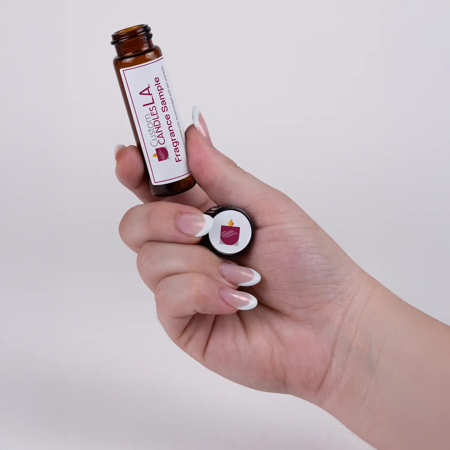 Hand holding two small bottles labeled 'Custom Candle LA' against a plain background