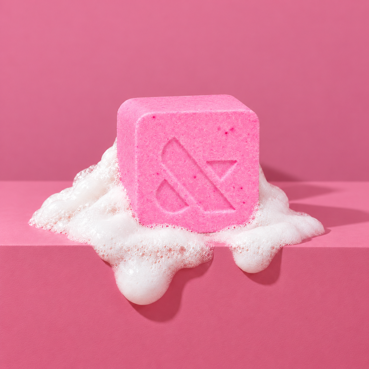 Pink custom bath bomb with a debossed brand logo on a pink backdrop, resting in white foam