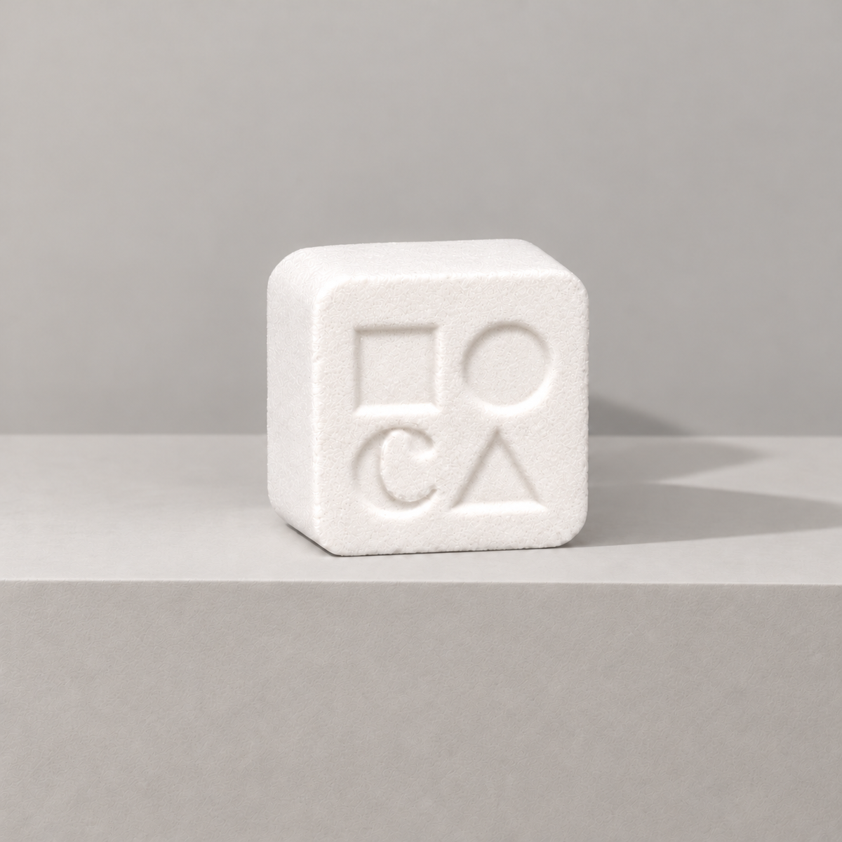 White custom bath bomb with a debossed brand logo on a gray backdrop, no foam