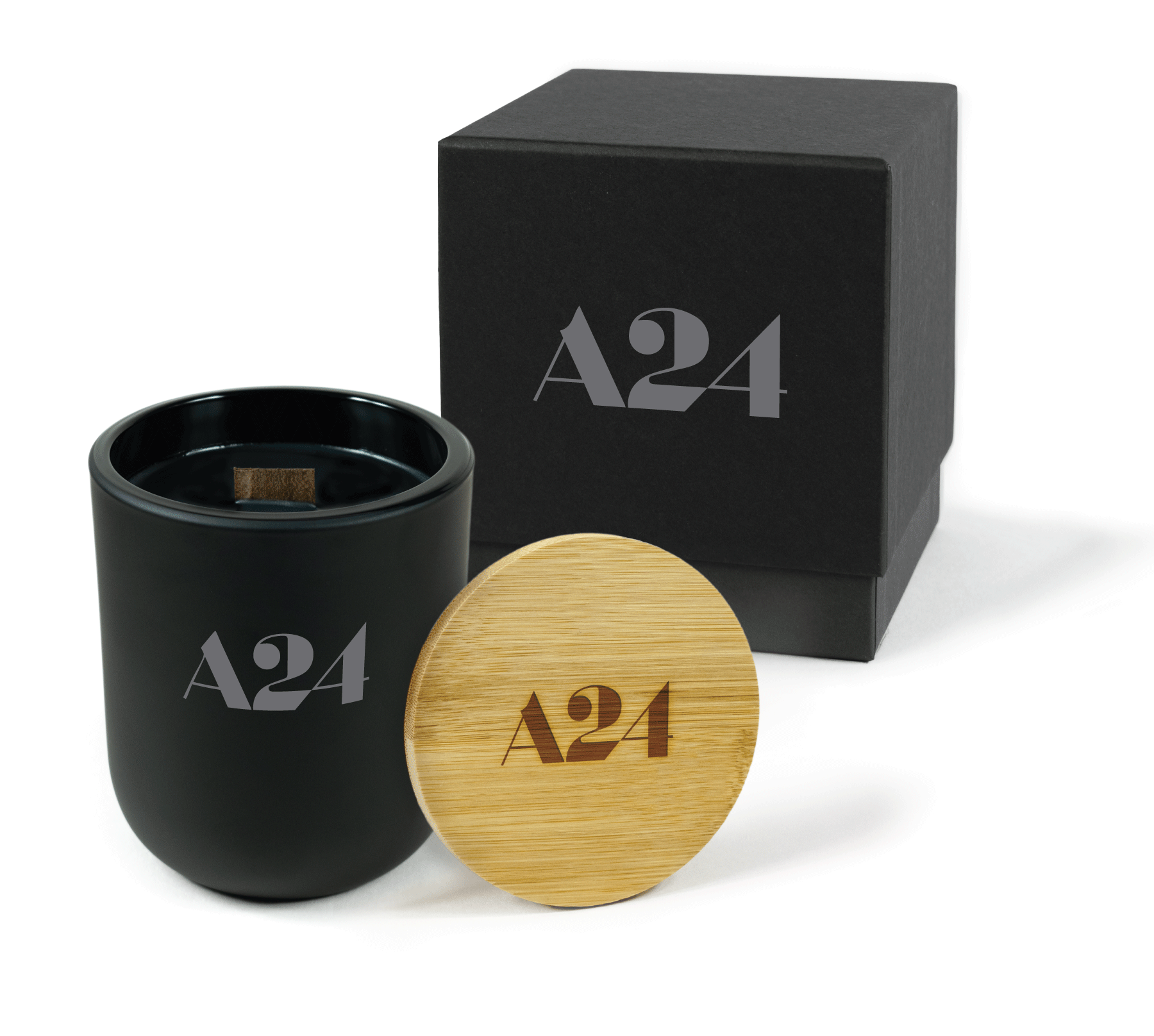 A 12 oz Luxe Custom Candle in the color “Darkest Night” which is jet black from Custom Candles LA. The candle features a wood wick and gray 4-color imprinted logo for “A24" on the front of the glass. Leaning against the side of the candle is a bamboo candle lid etched with the “A24” logo. In the background, there is a black 2-piece box 4-color printed with a grey “A24" logo.