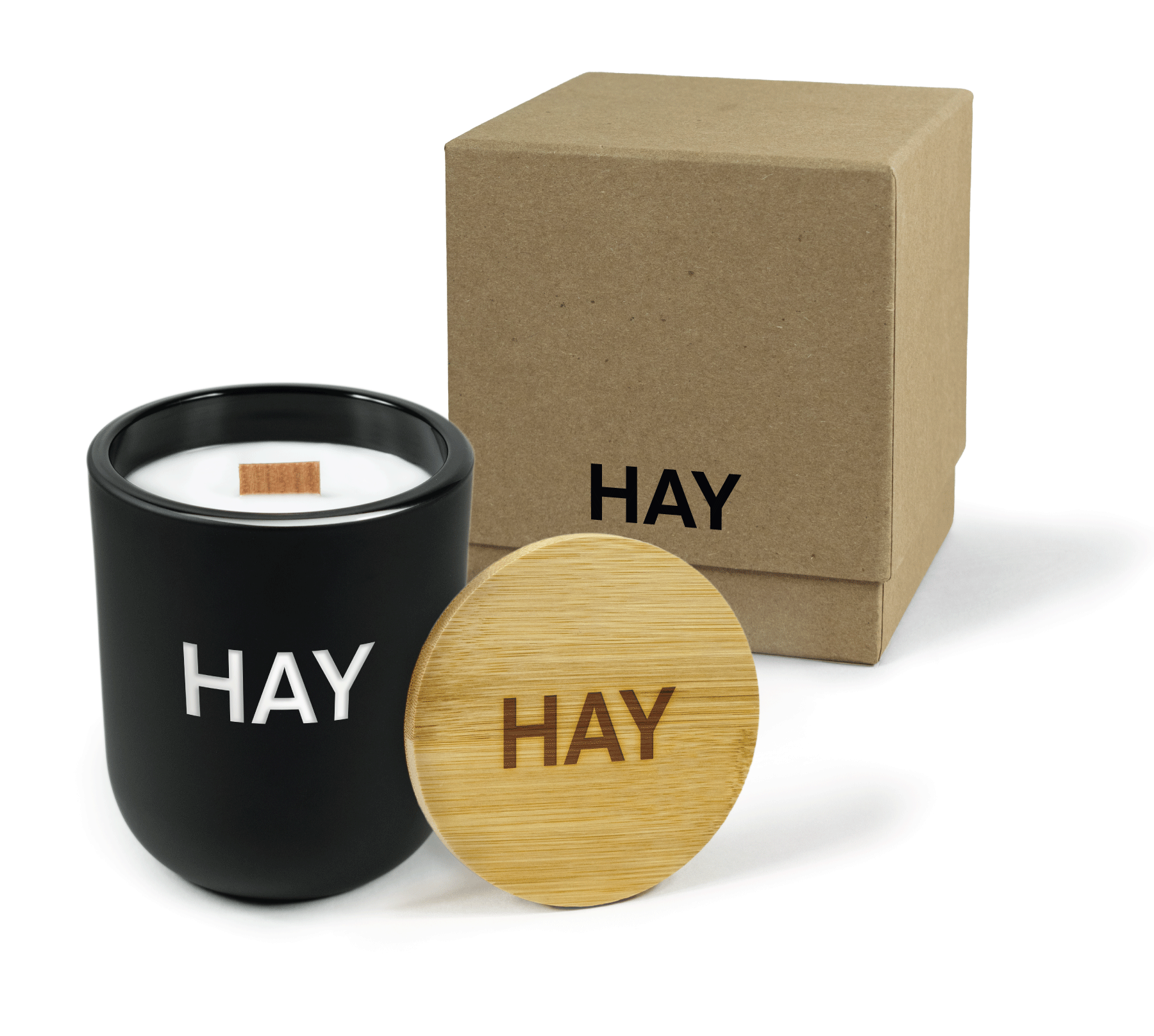 A 12 oz Luxe Custom Candle in the color “Darkest Night” which is a jet black from Custom Candles LA. The candle features a wood wick and “HAY” logo engraved on the front of the glass showing the white wax of the candle.. Leaning against the side of the candle is a bamboo candle lid etched with the “HAY” logo. In the background, there is a kraft 2-piece box printed with a small black “HAY” logo.