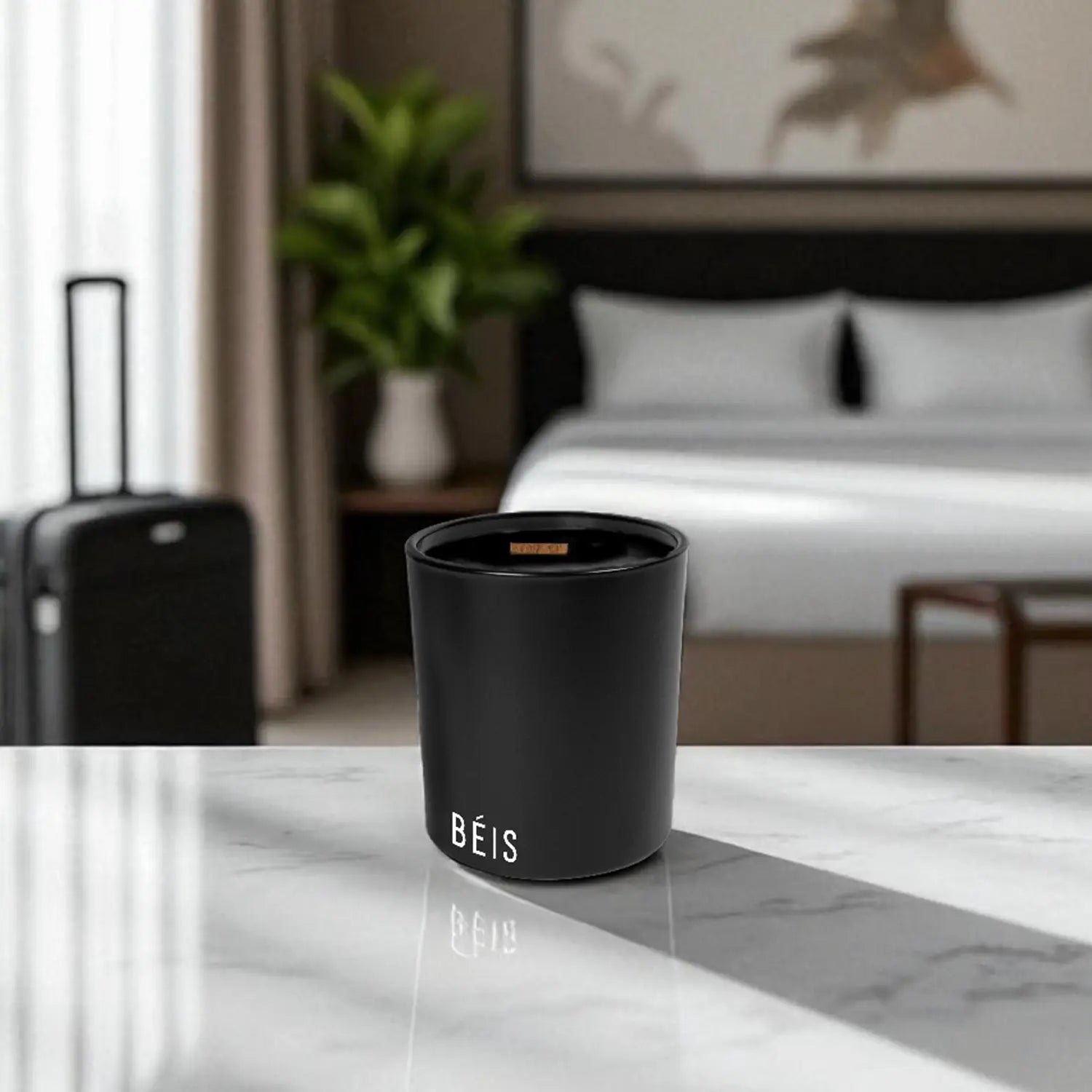 Black candle with printed logo on a marble surface, with a bedroom in the background.