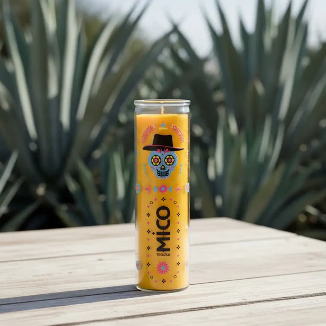 candle with colorful design on a wooden surface with agave plants in the background