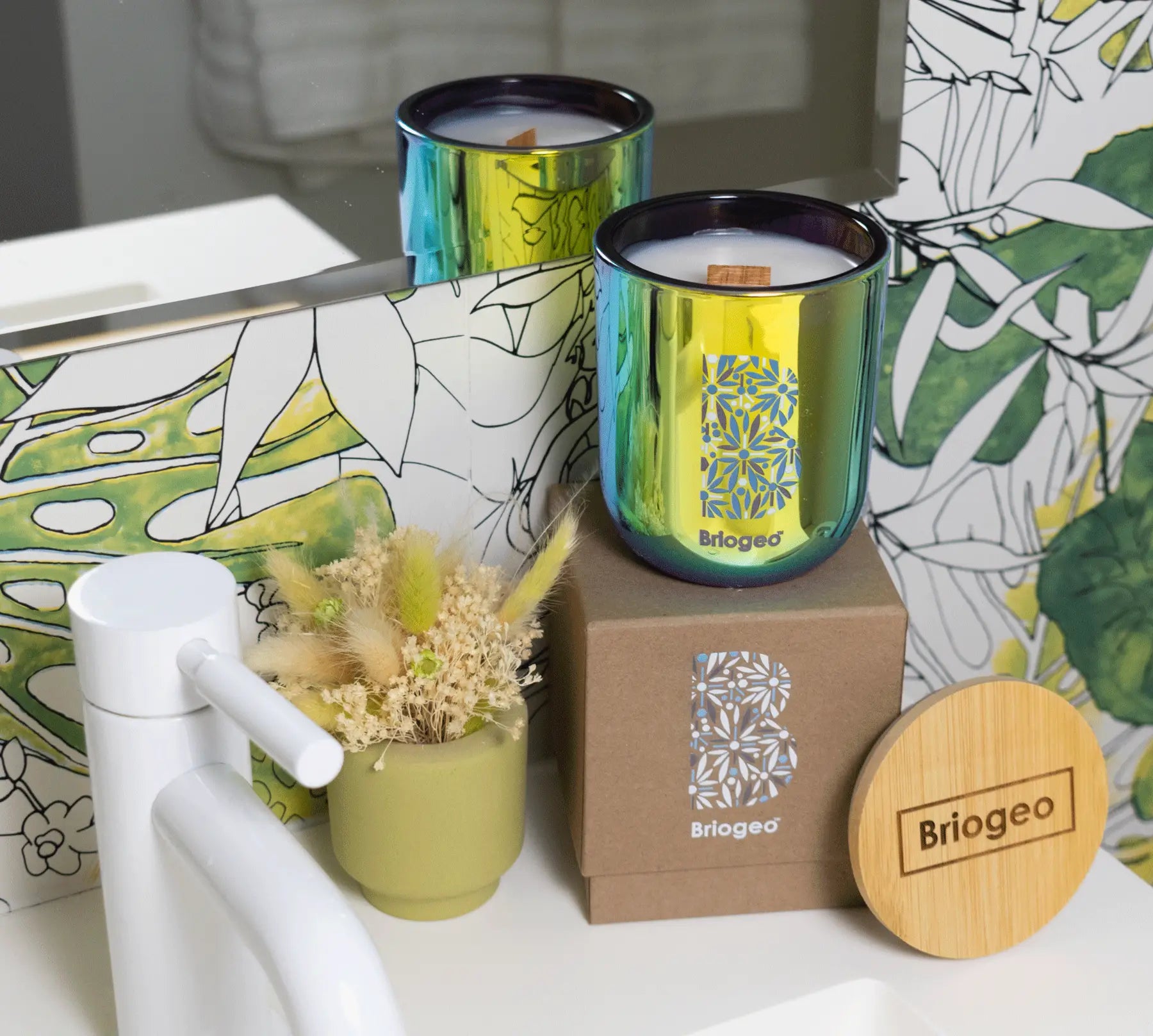 Two candles with decorative packaging on a surface with a floral design.