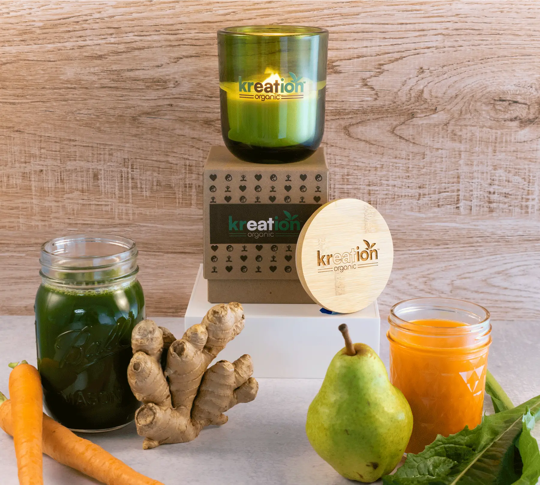 Green custom candle product shot with jars of juice, and fresh produce on a wooden surface.