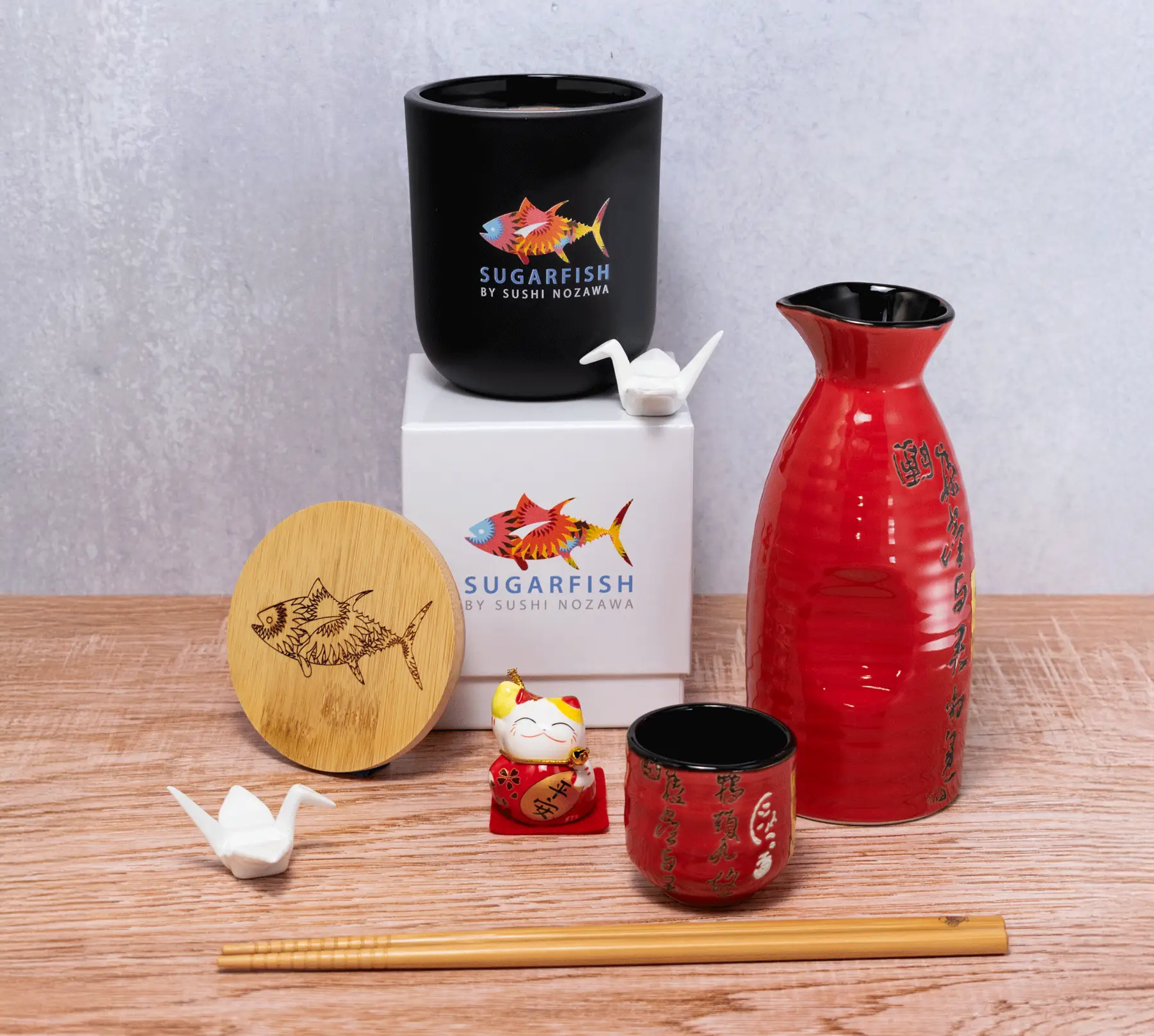 Collection of an image with a fish branded items including a red vase, black cup, and wooden lid on a wooden surface.