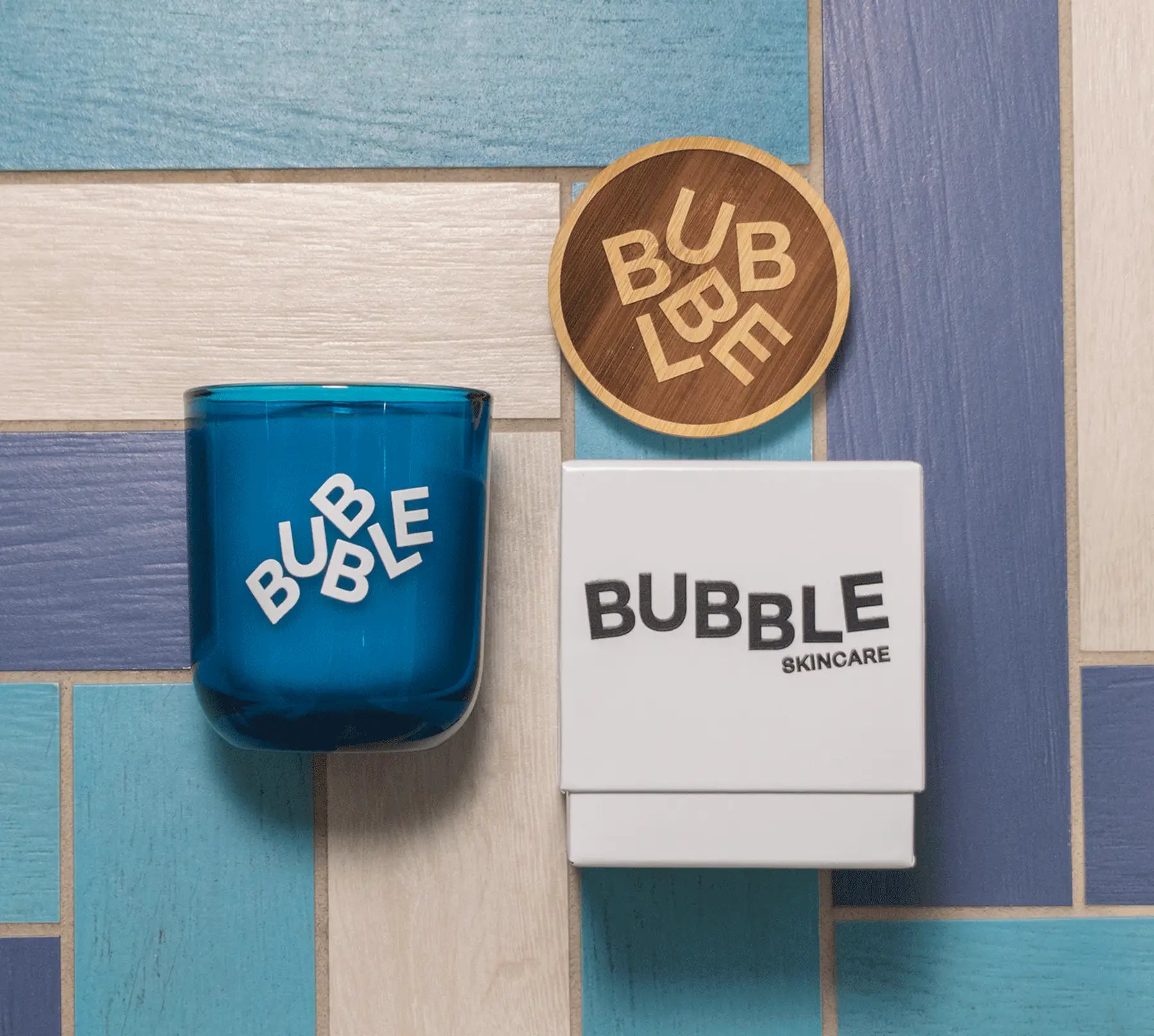 Blue glass, white box, and wooden coaster with logo branding on a multicolored wooden surface.