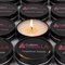 Several black tins labeled "Custom Candles L.A. Fragrance Sample" are arranged in rows. The center tin is open, revealing a lit candle with a single flame.