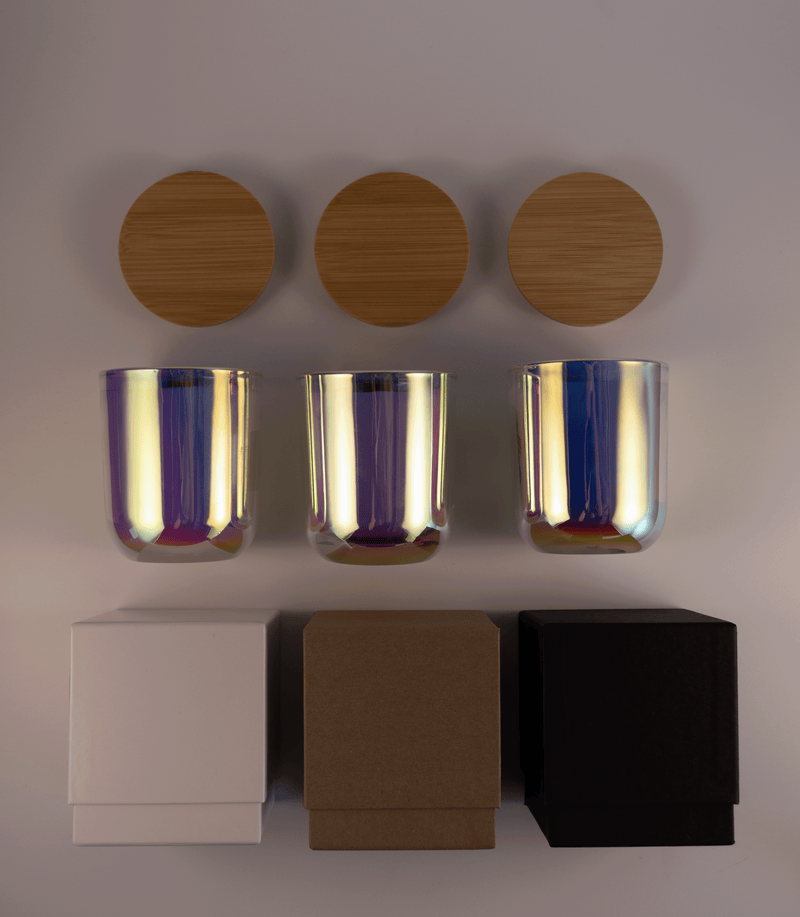Three iridescent pink glass tumblers with wooden lids above and three different boxes; white, kraft, and black; on a white surface.