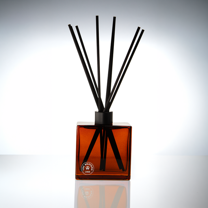 Amber glass 8 oz reed diffuser with black reeds on a soft gray backdrop