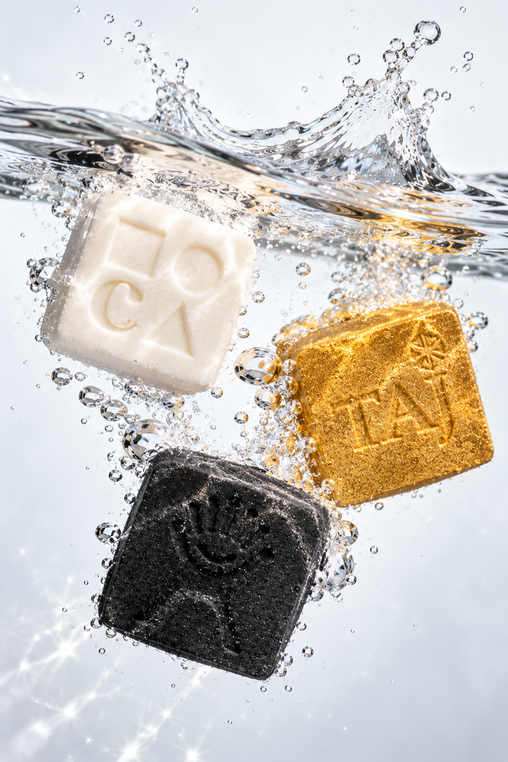 Three square bath bombs with debossed logos splashing into clear water