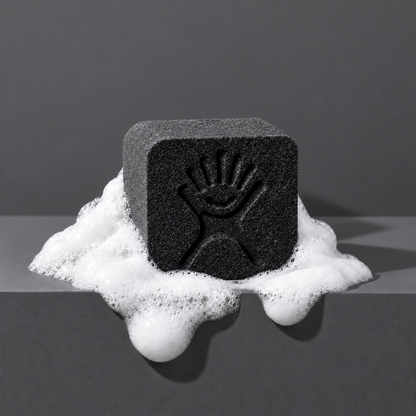Black custom bath bomb with a debossed brand logo on a dark gray backdrop, resting in white foam