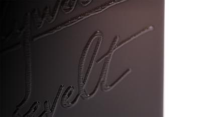 Close-up of a black tone-on-tone printed logo on a matte black reed diffuser bottle, catching the light.