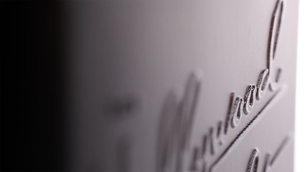 Close-up of a black-on-black script logo catching a soft edge of light