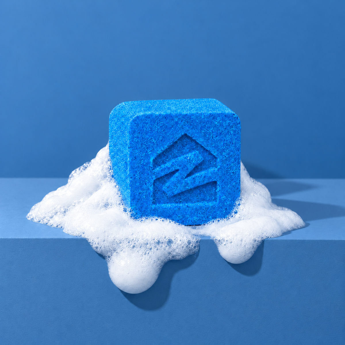 Blue custom bath bomb with a debossed brand logo on a blue backdrop, resting in white foam