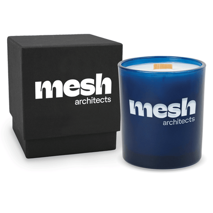 Blue 14 oz colored glass engraved logo candle beside a matte black gift box on a white background.
