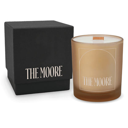 Sand 14 oz colored glass engraved logo candle beside a matte black gift box on a white background.