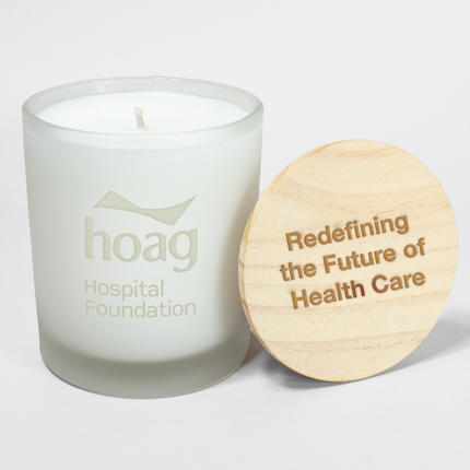 A 9 oz Standard "Design Your Own" Candle in an frosted white glass vessel from Custom Candles LA. The candle features an etched logo reading "hoag Hospital Foundation" on the glass vessel and a wooden lid engraved with the text "Redefining the Future of Health Care".