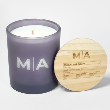 The "Monogram For The Record" candle is featured in a frosted lavendar candle from Custom Candles LA, with the monogram "M|A" etched into the glass with white wax showing through. The lid is engraved with the monogram "M|A" following by a box filled with details about a first date.