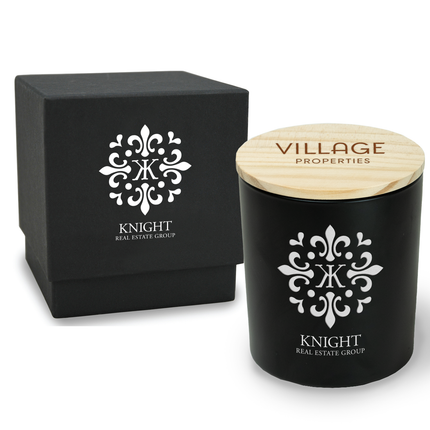 A 14 oz Deluxe "Design Your Own" Candle in a black glass vessel from Custom Candles LA. The candle features an etched logo that reads "Knight Real Estate Group" on the glass vessel and a black wooden lid imprinted with white text that reads "Village Properties".  Behind the candle is a 2 piece black box with a logo that reads "Knight Real Estate Group" printed in white. 