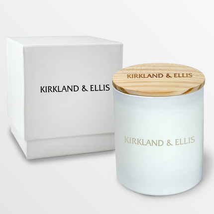 A 14 oz Deluxe "Design Your Own" Candle in a matte white glass vessel from Custom Candles LA. The candle features an etched logo reading "Kirkland & Ellis" on the glass vessel and a wooden lid imprinted with the text "Kirkland & Ellis".  Behind the candle is a 2 piece white box with a the logo "Kirkland & Ellis" in black.