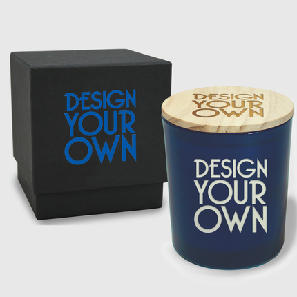 A customizable black candle container—named the Design-Your-Own Etched Custom Candle—Premium by Custom Candles LA and featuring "DESIGN YOUR OWN" in blue text—sits beside a sleek black box adorned with the same phrase. The candle boasts a wooden lid, also etched with "DESIGN YOUR OWN," creating a modern and elegant aesthetic against a white background.