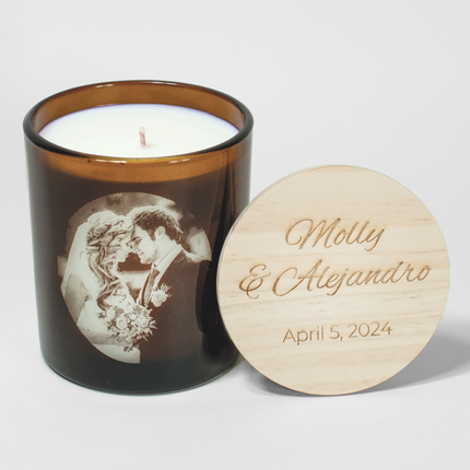 Wedding Photo 14 oz. Candle in amber glass from Custom Candles LA filled with white wax and a photo of a bride and groom etched into the candle. Next to it is a wooden lid engraved with the text "Molly & Alejandro April 5, 2024"