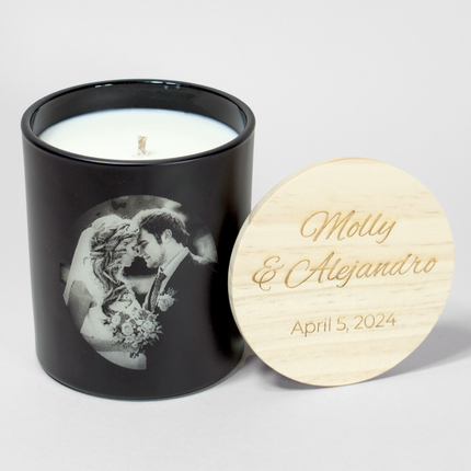 Wedding Photo 14 oz. Candle in matte black from Custom Candles LA filled with white wax and a photo of a bride and groom etched into the candle. Next to it is a wooden lid engraved with the text "Molly & Alejandro April 5, 2024"