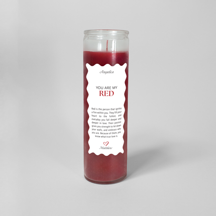 A tall cylindrical candle in a glass container filled with red wax titled "You are my RED" on a white label with scalloped edges. The label also includes a note explaining what the color red represents followed by a red heart at the bottom.