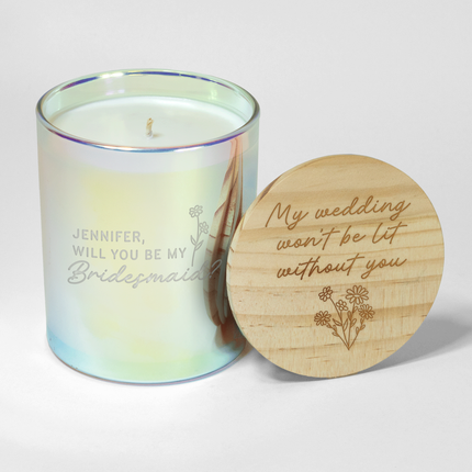 Custom Candles LA offers a charming Bridal Party Candle in a glass container, personalized with "Jennifer, will you be my bridesmaid?" engraved on the candle with a stemmed flower next to it. The accompanying wooden lid features the heartfelt message "My wedding won't be lit without you" along with an elegant floral design—making it the perfect wedding party gift.