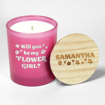 The "Will you be my Bridesmaid?" candle is a hot pink candle from Custom Candles LA, featuring white wax and a white wick and labeled "Will you be my Flower Girl?" in a funky font with decorative flowers surrounding; it comes next to a wooden lid engraved with the name "Samantha" and floral designs, making it an ideal wedding party gift.