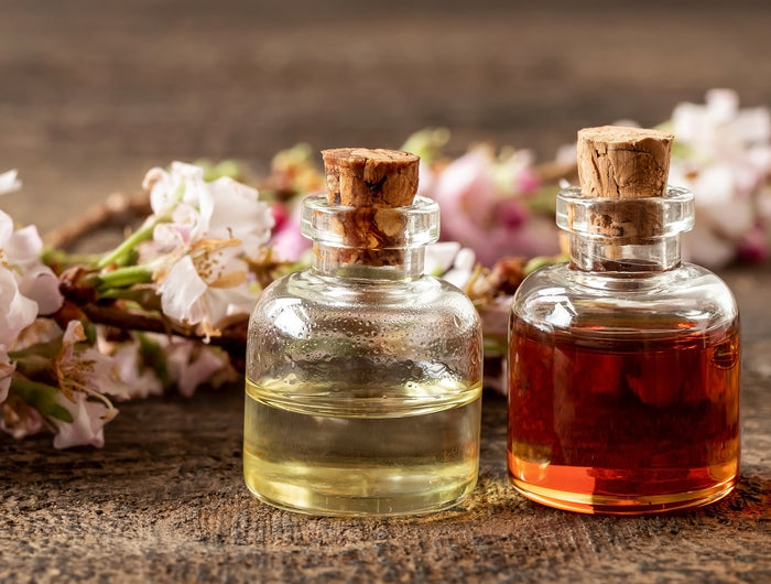 3 glass vials filled with liquid and cork stoppers. They sit on a brown wooden floor with pink and green flowers fill the background.