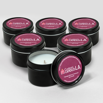 Six-pack of black tins of 2 oz Sample Fragrance Travel Candles from Custom Candles LA. The candle in front has its lid off of the sample tin and off to the side. 