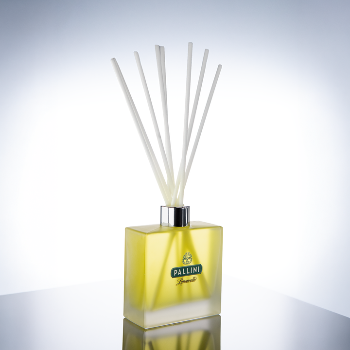 Square frosted pale yellow glass reed diffuser with a small dark green logo, white reeds and a silver collar