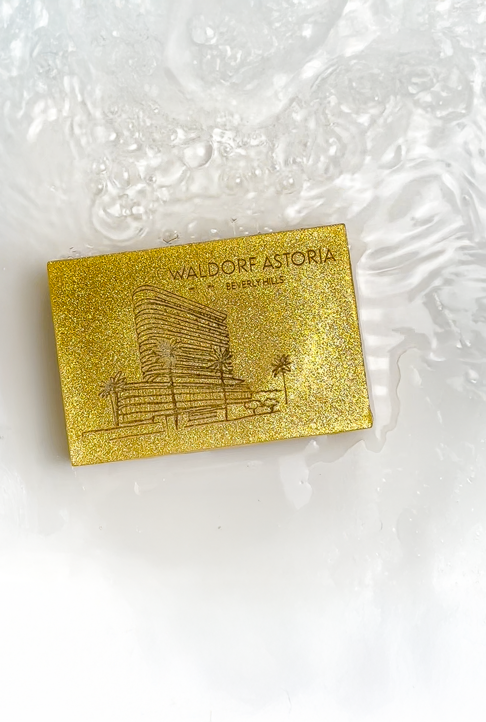 Gold rectangle bar soap engraved with a building illustration resting in clear water