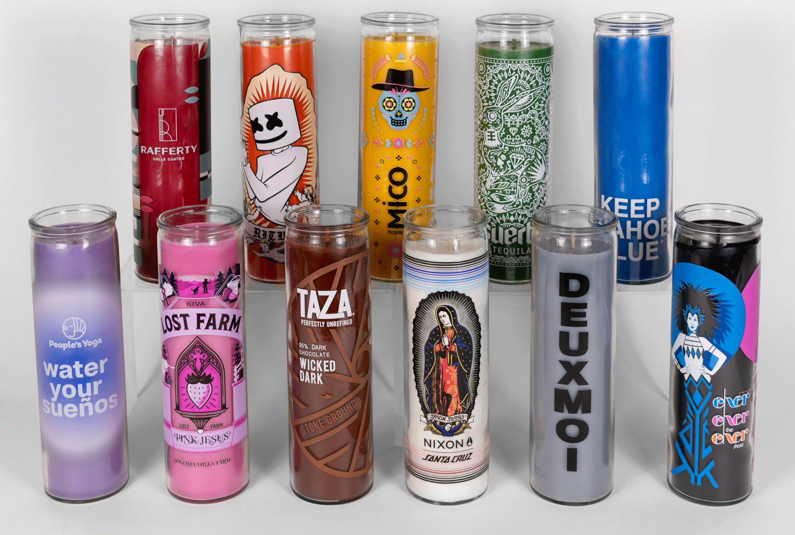 An assortment of 16 oz. 7-day Custom Prayer Candles from Custom Candles L.A. Each candle is a different color. From left to right on the top row the order is: Red, orange, yellow, green blue. From left to right on the bottom row the order is: purple, pink, brown, white, gray, black. Each candle has a unique logo and artwork printed on it. 