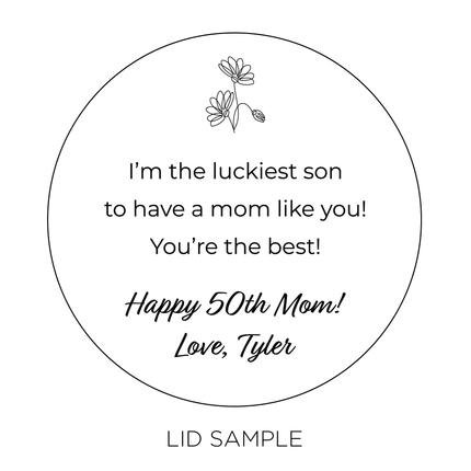 A sample of the wooden lid for the "I Love You Mom" Candle by Custom Candles L.A. features the message "I'm the luckiest son to have a mom like you! You're the best! Happy 50th Mom! Love, Tyler" along with an illustration of small flower at the top of the lid.