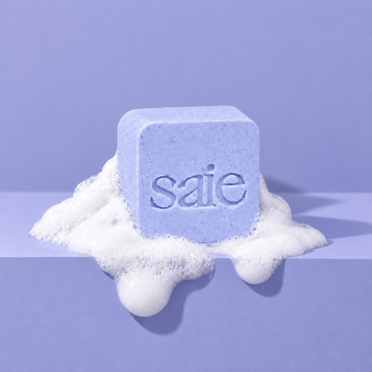 Lavender custom bath bomb with a debossed brand logo on a lavender backdrop, resting in white foam