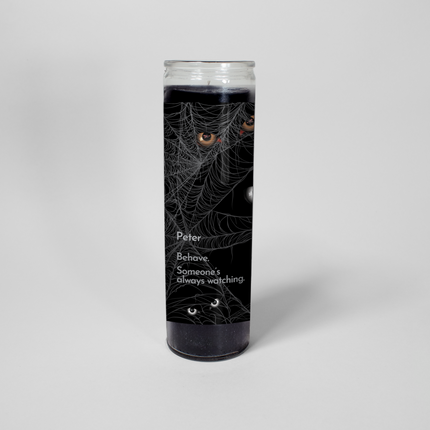 This Halloween-themed prayer candle from Custom Candles LA features a black jar with a spooky design. The text "Peter, Behave. Someone's always watching" is printed on the candle, surrounded by images of spider webs and eyes. This is the Always Watching candle.