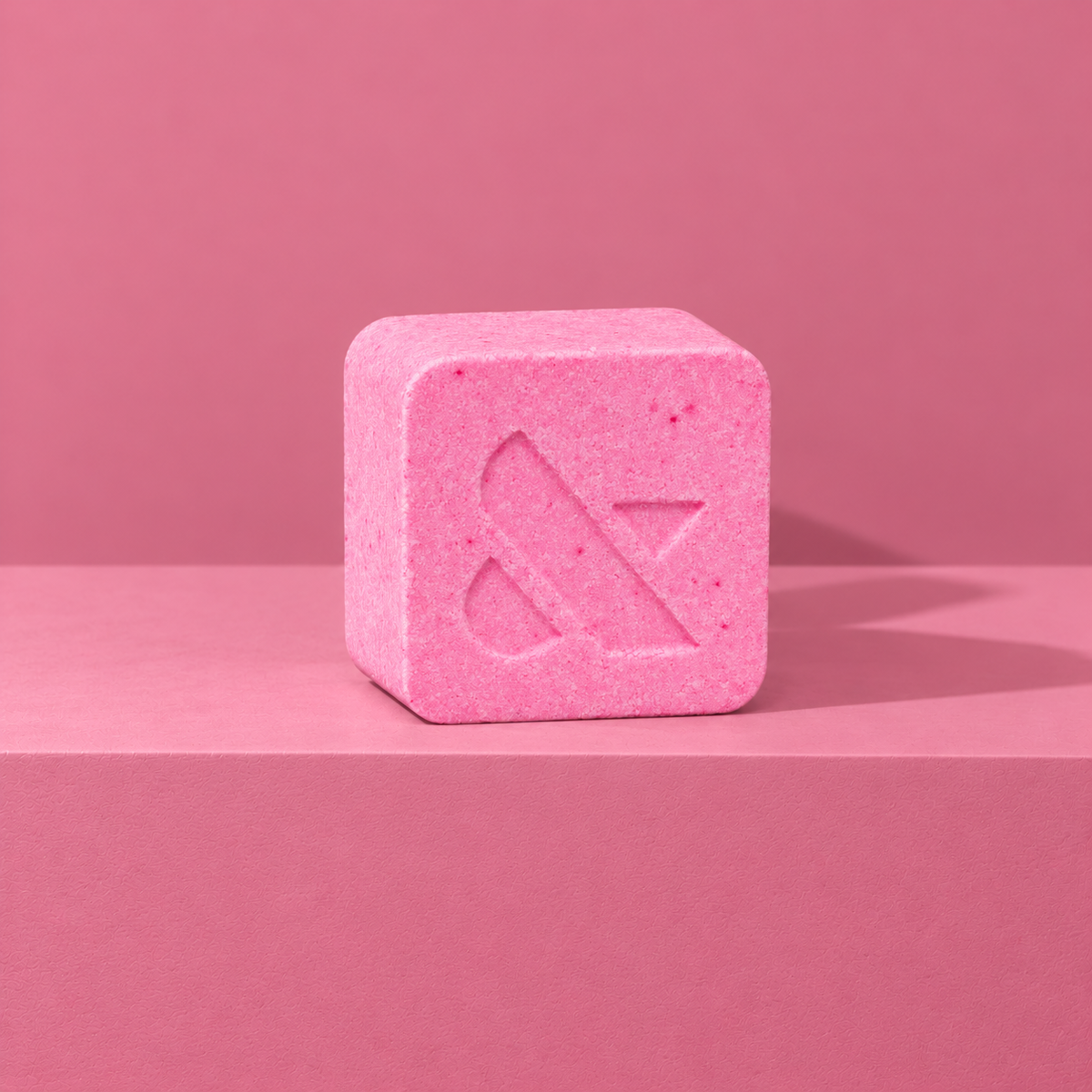 Pink custom bath bomb with a debossed brand logo on a pink backdrop, no foam