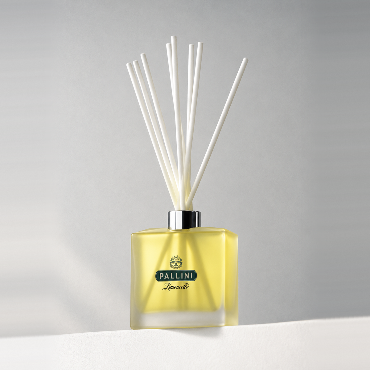 Pale yellow-tinted glass 8 oz. reed diffuser with white reeds and a printed logo, on a white ledge against a soft gray backdrop