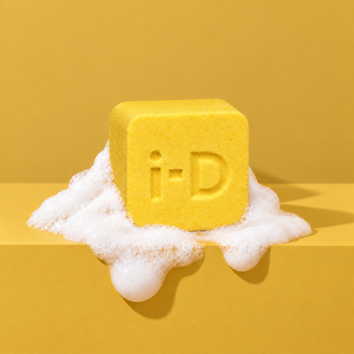 Yellow custom bath bomb with a debossed brand logo on a yellow backdrop, resting in white foam
