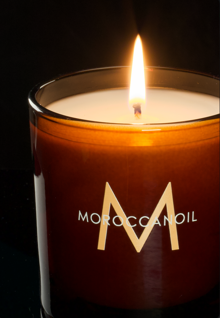 Glossy amber 9 oz candle with a custom printed gold logo, lit