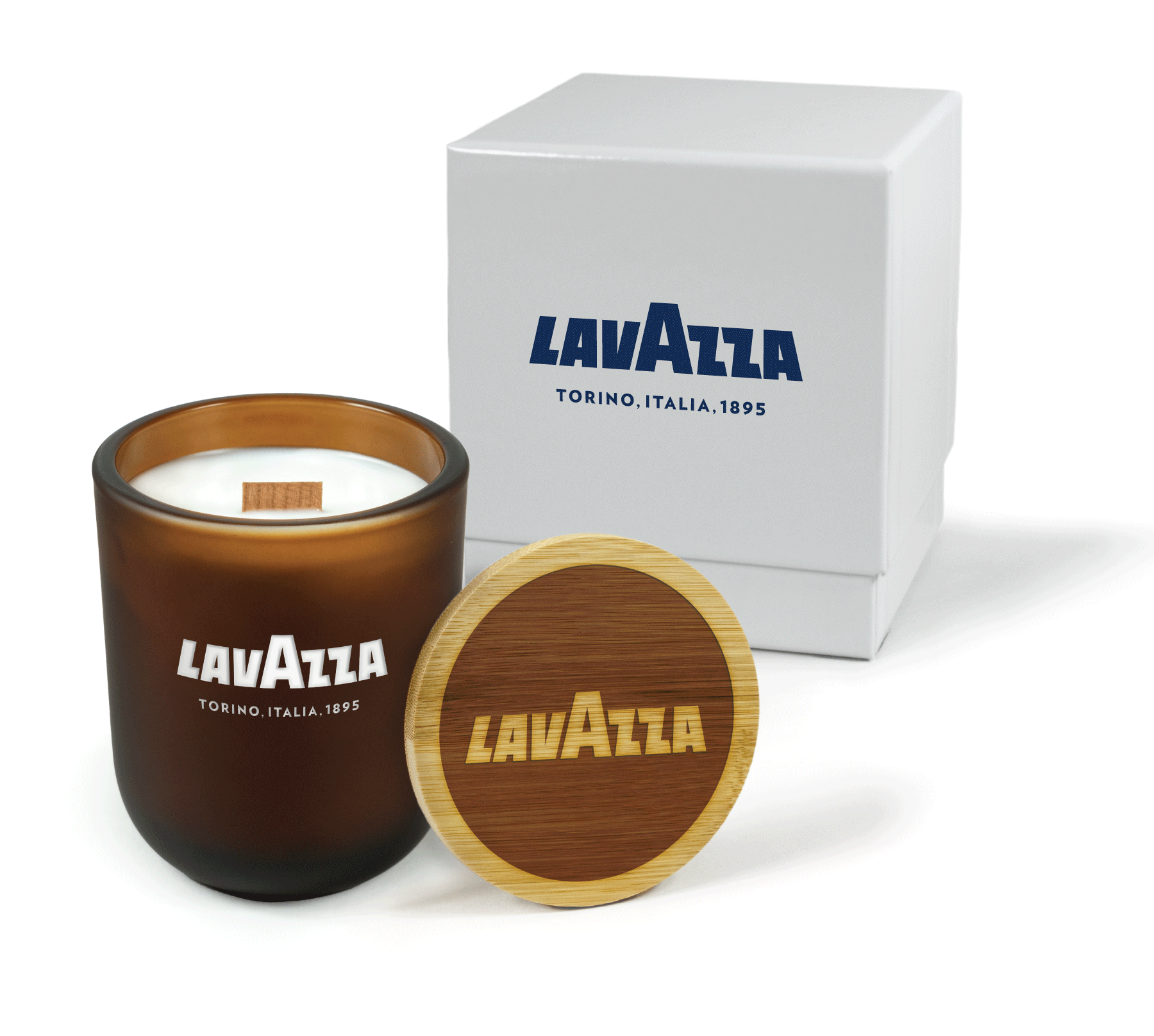 A 12 oz Luxe Custom Candle in the color “Cacao” which is an amber brown from Custom Candles LA. The candle features a wood wick and “Lavazza Torina. Italia. 1895” engraved on the front of the glass showing the white wax of the candle. Leaning against the side of the candle is a bamboo candle lid etched with the the “Lavazza” logo. In the background, there is a white 2-piece box printed with blue logo for “Lavazza” above text reading “Torina. Italia. 1895".