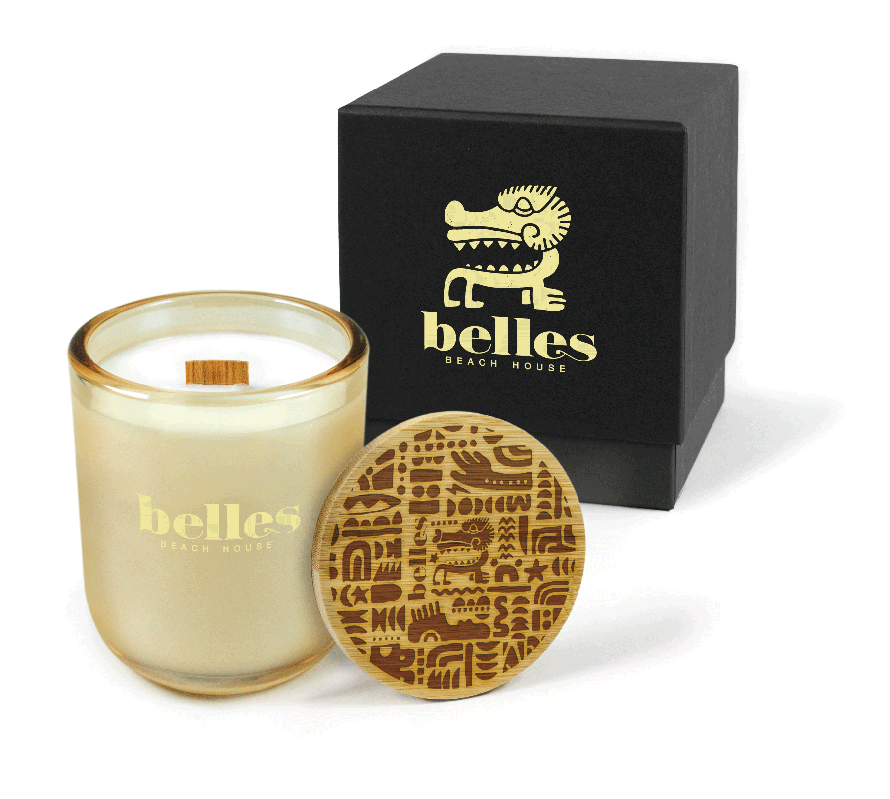 A 12 oz Luxe Custom Candle in the color “Daybreak” which is a glimmering gold from Custom Candles LA. The candle features a wood wick and pale yellow 4-color imprinted logo for “Belles Beach House” on the front of the glass. Leaning against the side of the candle is a bamboo candle lid engraved with the “Belles” logo and an abstract pattern. In the background, there is a black 2-piece box 4-color printed with a pale yellow “Belles Beach House” logo and icon.