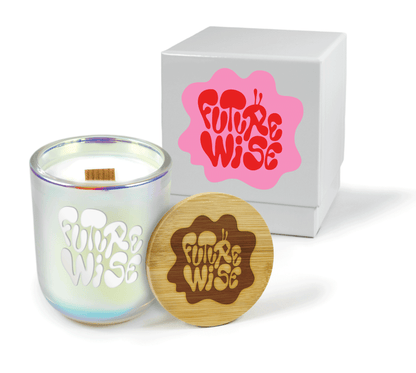 A 12 oz Luxe Custom Candle in the color “Bliss” which is an iridescent pink from Custom Candles LA. The candle features a wood wick and an engraved logo for “Future Wise” on the front of the glass showing the white wax of the candle. Leaning against the side of the candle is a bamboo candle lid etched with the “Future Wise” logo. In the background, there is a white 2-piece box printed with a pink and white “Future Wise” logo.